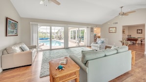 A spacious living room with a pool view, a ceiling fan, and a pool table.