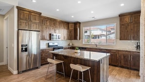 A modern kitchen with wooden cabinets, stainless steel appliances, and a large island with bar stools. - Red Sand Hideaway #119 5 Bedroom Home (Ivins)