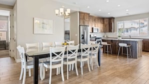A modern kitchen with wooden cabinets, a central island, and a dining area with white chairs. - Red Sand Hideaway #119 5 Bedroom Home (Ivins)