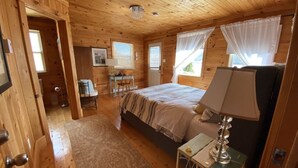 A wooden cabin bedroom with a bed, a desk, and a chair. - One bedroom two bath beach house over looking the ocean. (Trinity)
