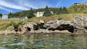 A rocky shoreline with clear water and a residential area in the background. - One bedroom two bath beach house over looking the ocean. (Trinity)