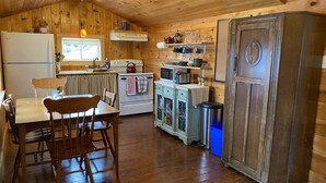A rustic kitchen with wooden walls, a wooden dining table with chairs, a refrigerator, a stove, a microwave, and a cabinet with glass doors. - One bedroom two bath beach house over looking the ocean. (Trinity)