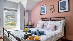A neatly made bed with a tray of breakfast items, a bedside table with a lamp, and a large window offering a view of the outdoors.