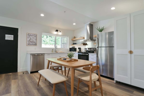 A modern kitchen with a wooden dining table, white cabinets, and stainless steel appliances. - Moab Inn Towner #3 - Heart of Downtown (Moab)