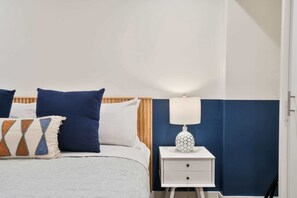 A neatly made bed with blue and white bedding, a bedside table with a lamp, and a nightstand.