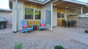 Ein modernes Haus mit überdachter Terrasse, Holzfassade und einem Essbereich mit Stühlen und Tisch.