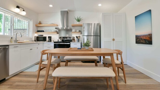 A modern kitchen with white cabinets, stainless steel appliances, and a wooden dining table with benches. - Moab Inn Towner #4 - Heart of Downtown (Moab)