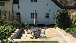 A white house with a thatched roof, a patio with a table and chairs, and a garden area. - Lime Cottage (Bridport)