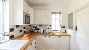 A compact kitchen with white cabinets, a microwave, a sink, and a window with a view. - Lime Cottage (Bridport)