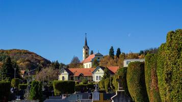 A cemetery with neatly trimmed hedges, a church with a tall steeple, and a hill in the background.