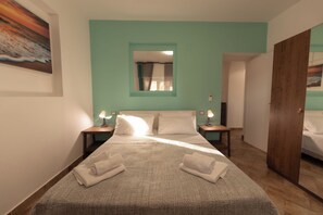A neatly made bed with white linens and towels, a teal-colored wall, and a painting of a sunset. - Apartment Poseidonia - Sole & Pepe - Santa Maria di Castellabate Cilento (Santa Maria di Castellabate)