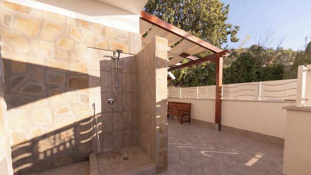 Zona de ducha con paredes de piedra, un banco y una estructura de pérgola.