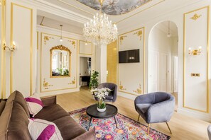 A luxurious living room with a chandelier, a sofa, a chair, and a colorful rug.