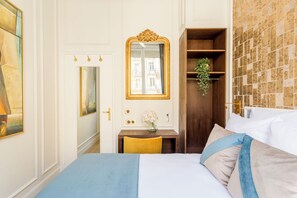A hotel room with a bed, a desk with a vase of flowers, a mirror, and a wardrobe.