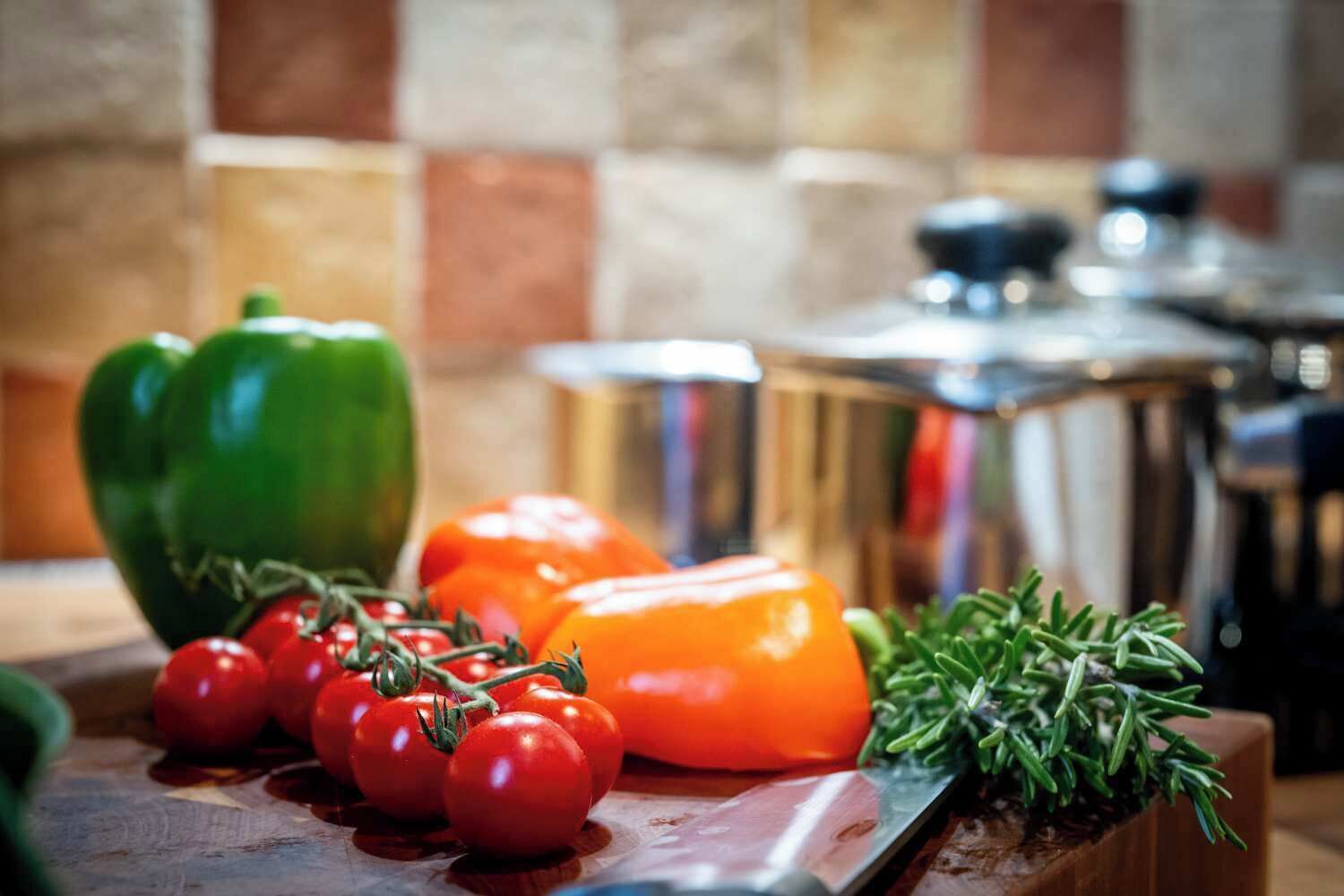 A kitchen counter with vegetables, a cutting board, and kitchen utensils.