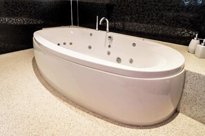 A large, oval-shaped bathtub with multiple faucets and a single showerhead, set against a dark patterned wall. - Sapphire - Spacious apartment near the Sea (Caister-on-Sea)