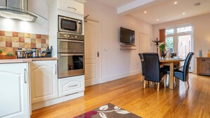 A modern kitchen with built-in appliances, a dining area with a table and chairs, and a TV mounted on the wall. - Sapphire - Spacious apartment near the Sea (Caister-on-Sea)