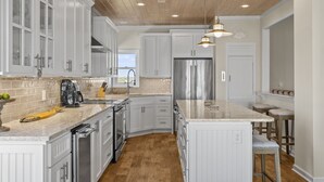 A modern kitchen with white cabinetry, a stainless steel refrigerator, and a wooden ceiling. - The Hamptons, Oceanfront Duplex in Atlantic Beach, NC! (Atlantic Beach)