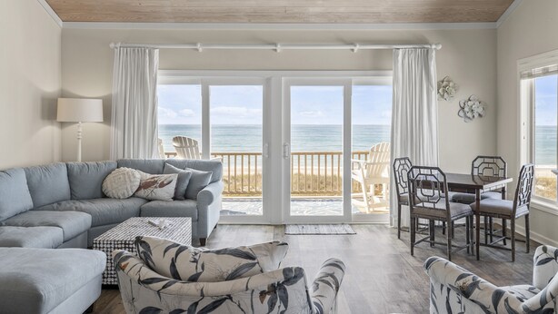 A living room with a sofa, armchair, and dining table, large sliding glass doors leading to a balcony with a view of the ocean. - The Hamptons, Oceanfront Duplex in Atlantic Beach, NC! (Atlantic Beach)