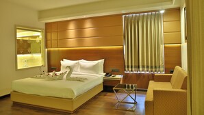 Quarto de hotel com uma cama grande, uma mesa de cabeceira com abajur, um sofá e uma mesinha de centro de vidro.