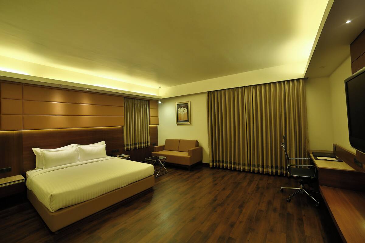 A hotel room with a large bed, a sofa, a desk, and a TV.