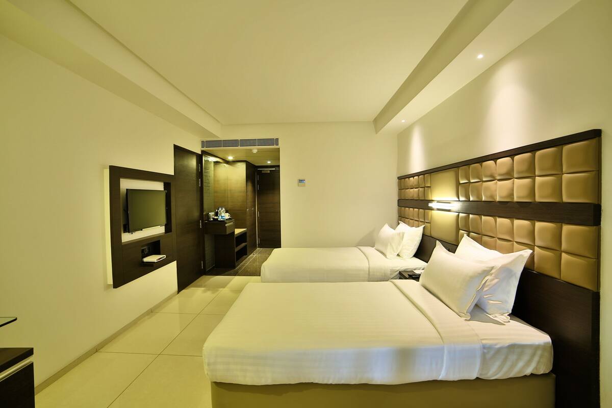 A hotel room with two beds, a TV, and a bathroom.