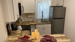 Una cucina moderna con mobili bianchi, un lavello in acciaio inossidabile e un frigorifero LG. Sono presenti due sgabelli gialli e un tavolo da pranzo in legno apparecchiato con piatti rossi e candele.