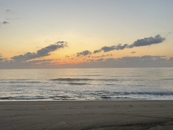 A beach at sunset with a clear sky and calm sea.