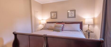 Un dormitorio con una cama de madera, dos lámparas de noche y cuadros en la pared.