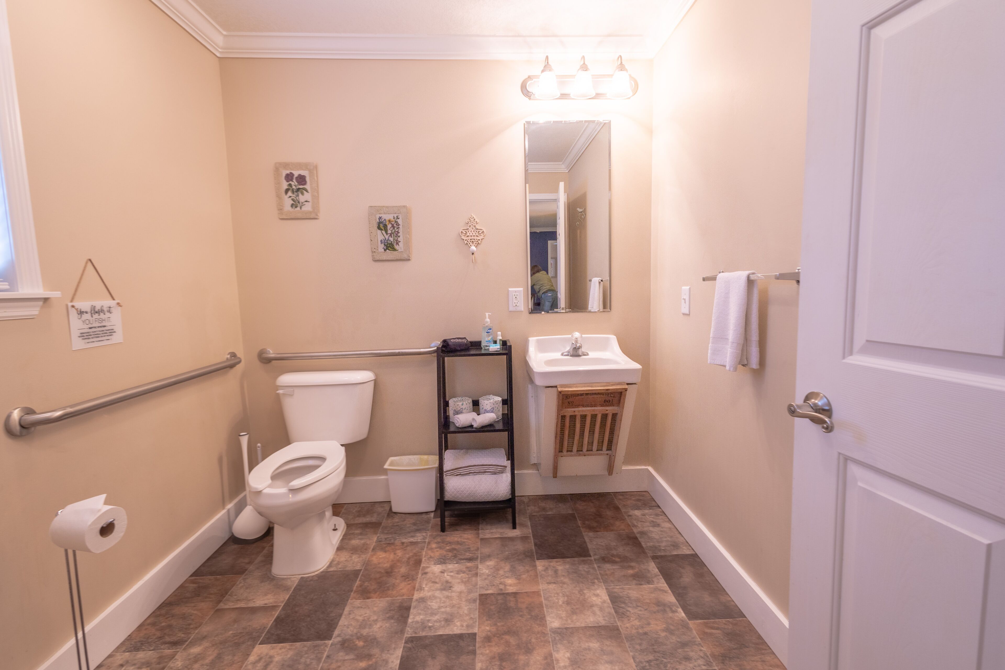 A bathroom with a toilet, sink, mirror, and a shelf with towels.