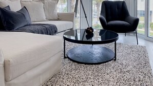 Un salon moderne avec un canapé, un fauteuil noir, une table basse et un lampadaire.