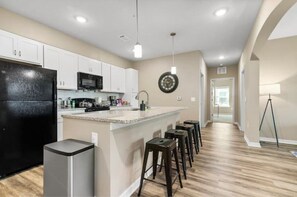 A modern kitchen with white cabinets, a black refrigerator, and a central island with bar stools. - Sophisticated 3BD/2BA Retreat: Pool, Gym, Laundry (Melbourne)