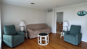 A living room with two teal armchairs, a beige sofa, and a round white coffee table. - Waterfront Rancher in South Bethany (Bethany Beach)