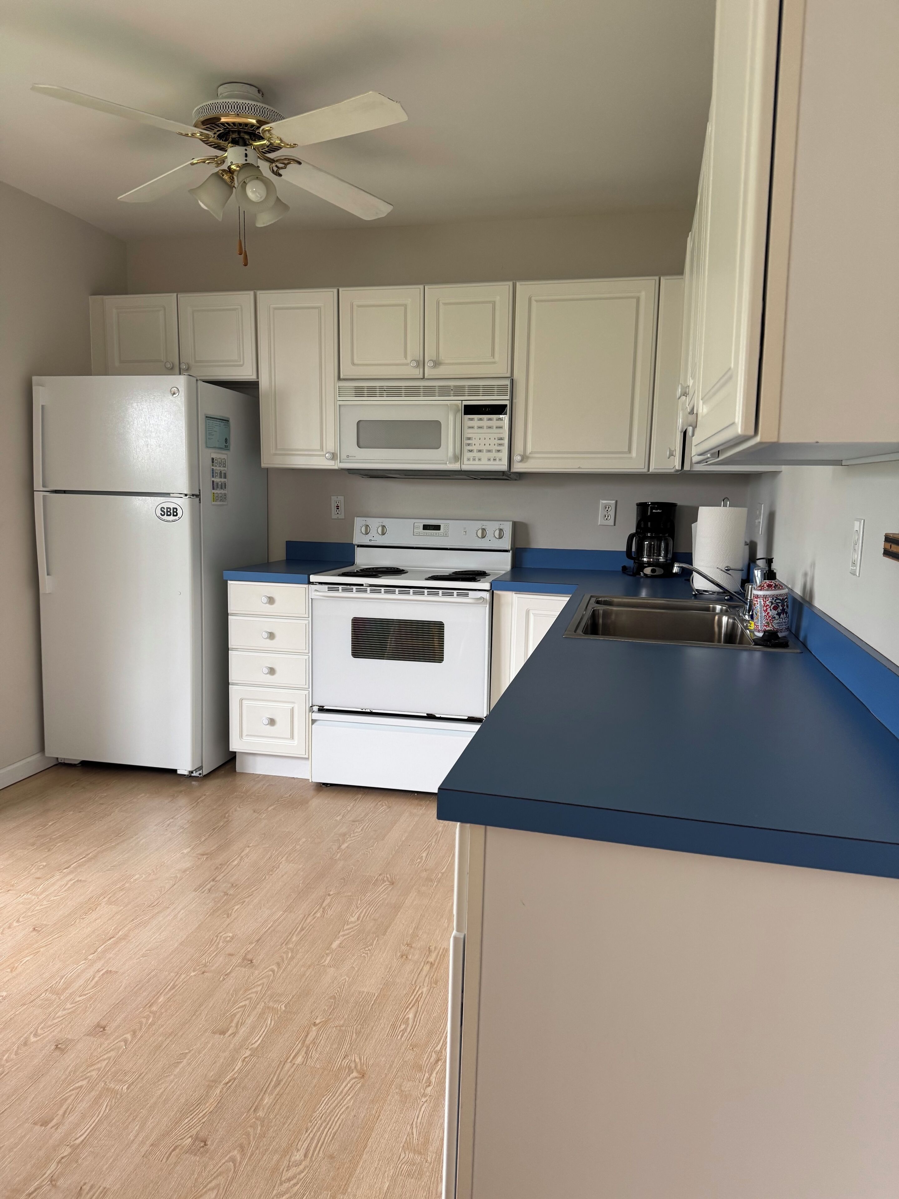 A kitchen with white cabinets, a white refrigerator, a microwave, a stove, and a ceiling fan.