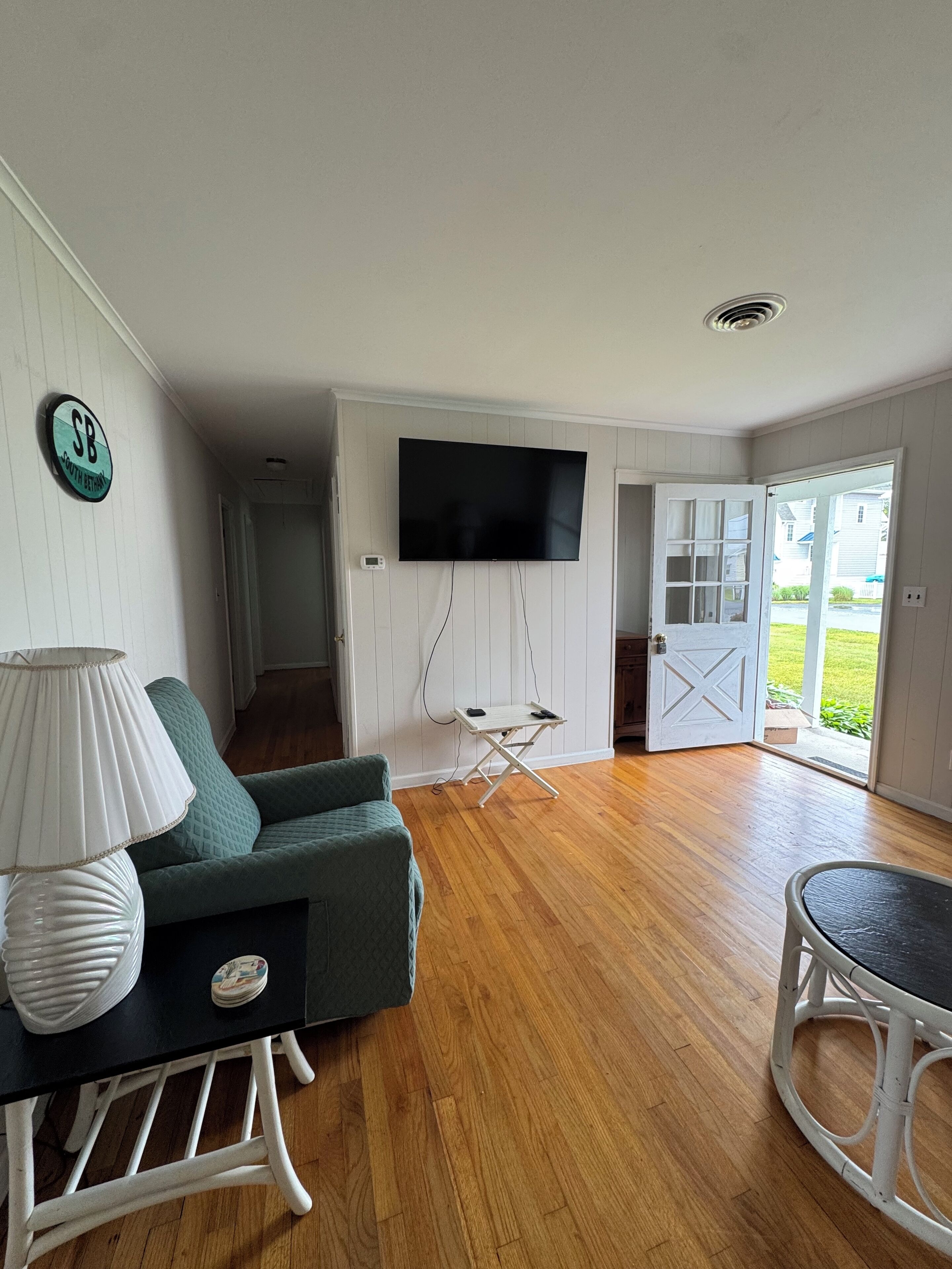 Un salón con un sofá verde, una lámpara blanca, un televisor de pantalla plana montado en la pared y piso de madera.