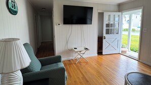 A living room with a green sofa, a white lamp, a flat-screen TV mounted on the wall, and a wooden floor. - Waterfront Rancher in South Bethany (Bethany Beach)
