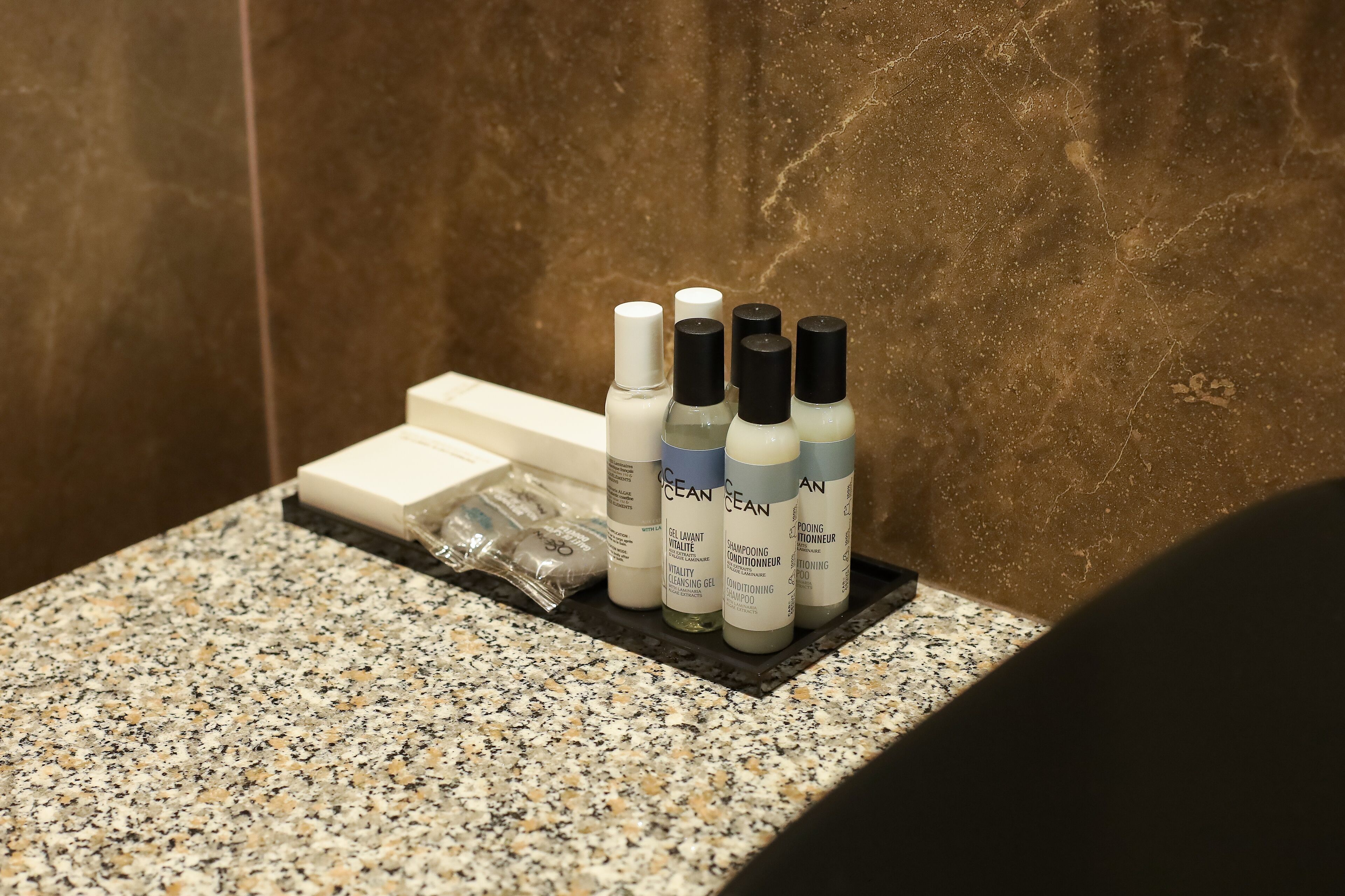 Un meuble-lavabo avec un plateau en marbre, sur lequel se trouvent une boîte blanche, un ensemble de quatre flacons étiquetés « Ocean Clean » et un petit sac en plastique.