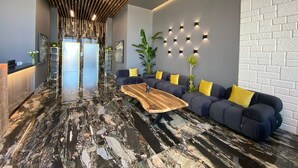 Un hall d’entrée moderne avec un comptoir de réception, un canapé d’angle avec des coussins jaunes, une table basse en bois et un sol en marbre à motifs.