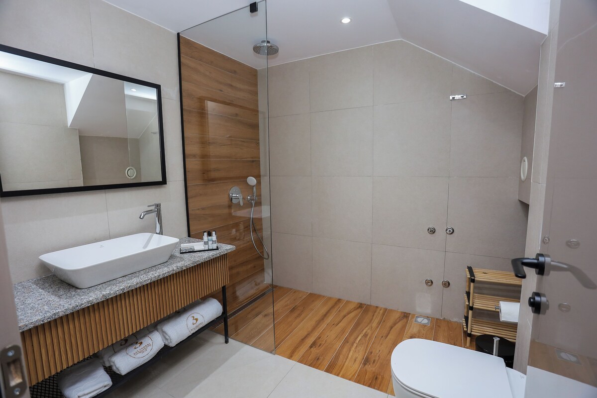 A modern bathroom with a large mirror, a white sink, a shower, and a toilet.