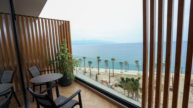 Un balcon avec vue sur la mer, des lambris en bois, une plante en pot et une table avec des chaises.