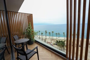 Un balcón con vista al mar, listones de madera, una planta en maceta y una mesa con sillas.