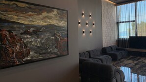 Un intérieur moderne agrémenté d’un grand tableau abstrait, d’un coin salon avec des canapés et d’une grande fenêtre avec des rideaux.