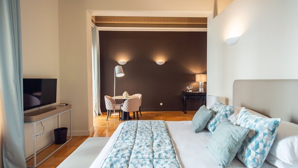 Ein Hotelzimmer mit einem großen Bett, einem Fernseher, einem Schreibtisch mit Lampe und einem Essbereich.