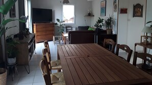 Un salon spacieux avec une table à manger en bois, des sièges confortables, un téléviseur à écran plat et diverses plantes.