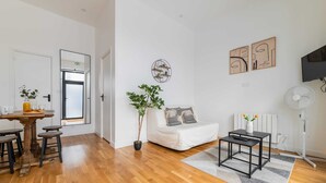 A modern living room with a white sofa, a dining table with stools, a potted plant, and a flat-screen TV mounted on the wall. - Appartement central a deux pas des Halles a Paris (Paris)