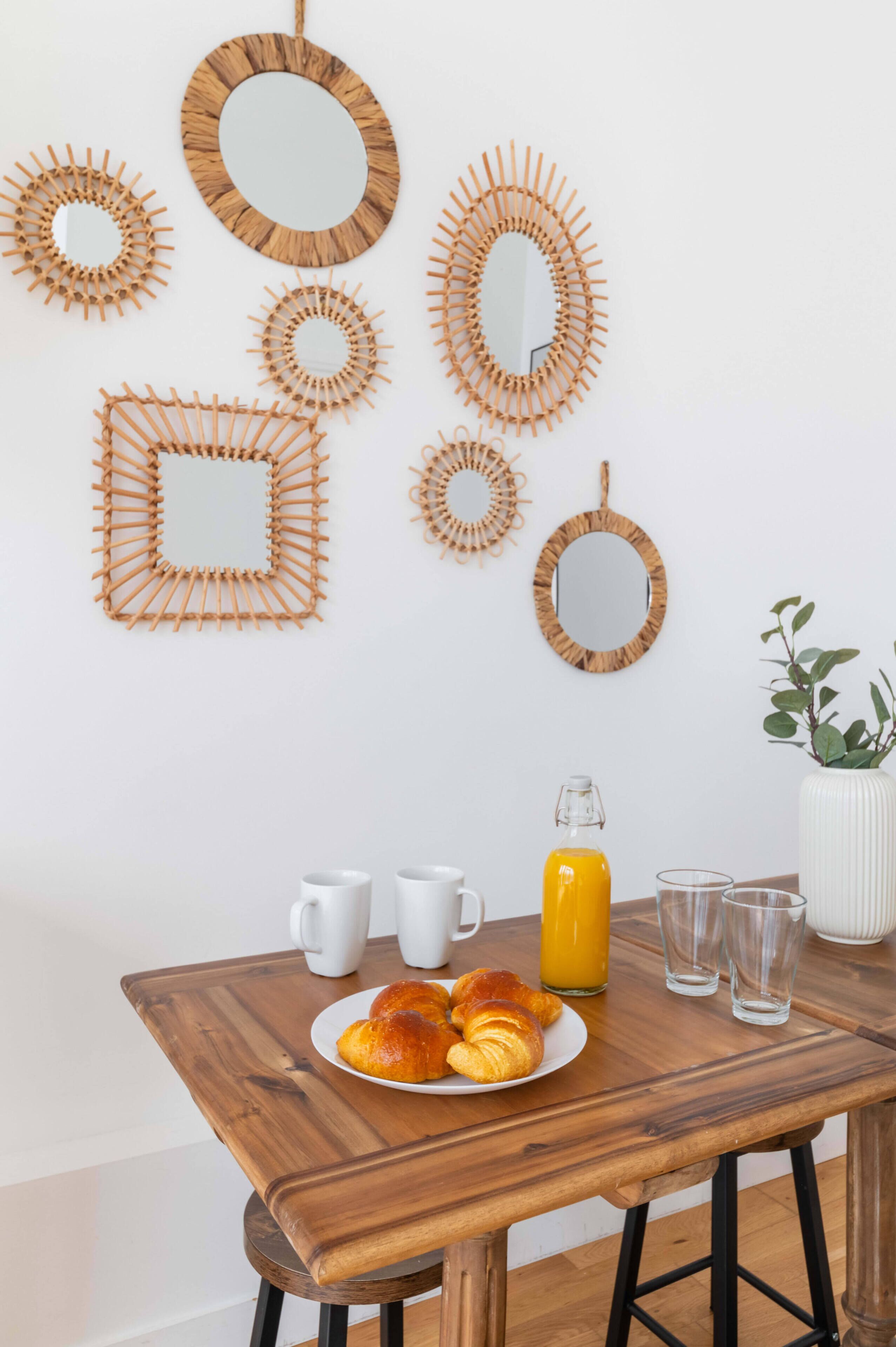 Una mesa de desayuno con cruasanes, una botella de jugo y vasos, rodeada de varios espejos en la pared.