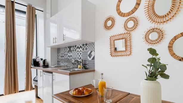 A modern kitchen with white cabinets, a patterned backsplash, and a wooden dining table with breakfast items. - Appartement central a deux pas des Halles a Paris (Paris)
