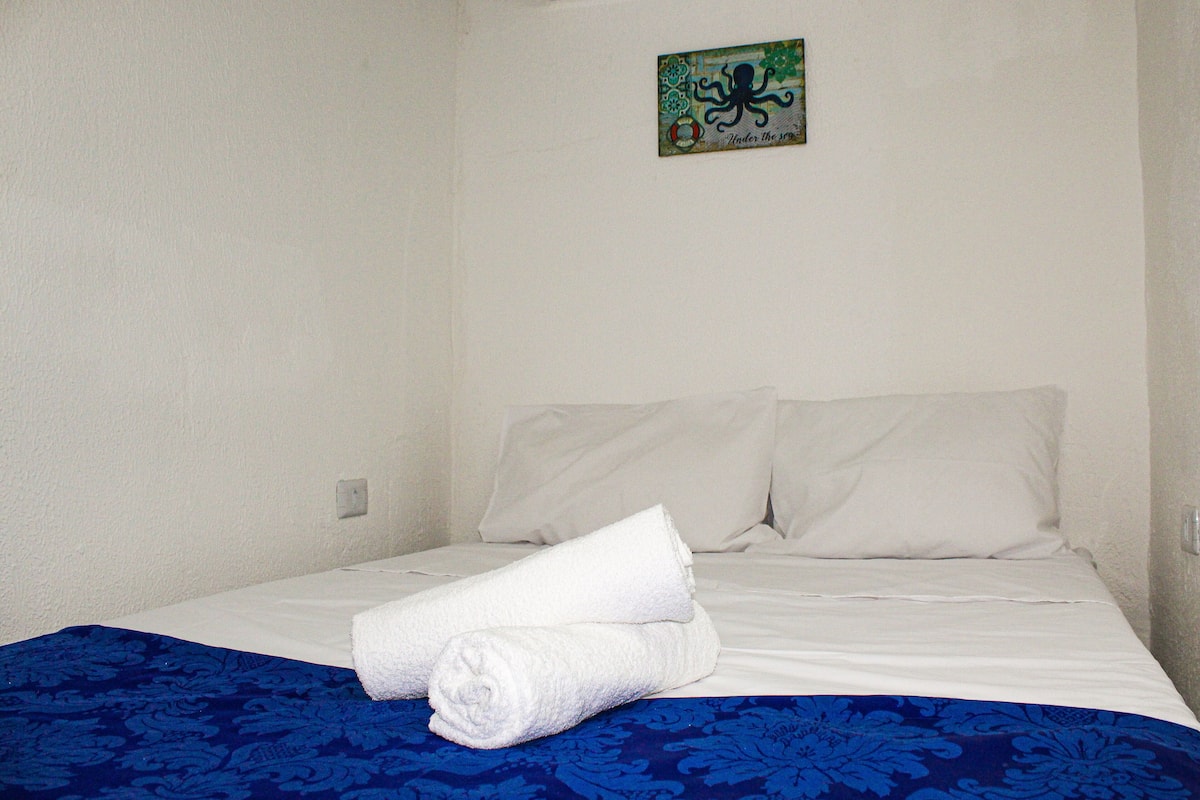 A neatly made bed with white linens and a blue patterned bedspread.