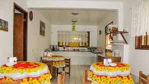 A dining area with two wooden tables covered with sunflower-patterned tablecloths, surrounded by wooden chairs. - Pousada Farol do Porto  (Ipojuca)