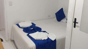 A single bed with white and blue bedding, a blue pillow, and a folded white towel on the bed. - Pousada Farol do Porto  (Ipojuca)